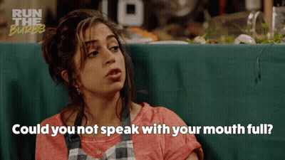 A Woman Sitting At A Table With The Words " Could You Not Speak With Your Mouth Full " Written Below Her GIF
