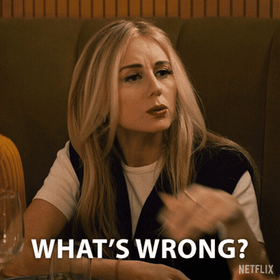 A Woman Sitting At A Table With The Words What 'S Wrong On The Bottom GIF