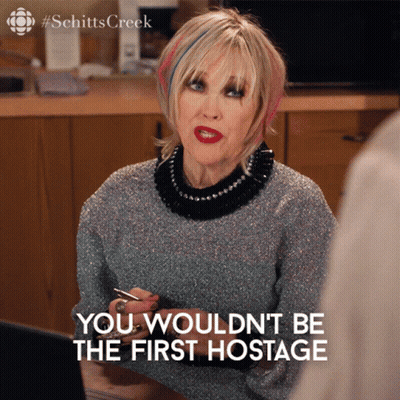 A Woman Sitting At A Table With The Words " You Would N't Be The First Hostage " Below Her GIF