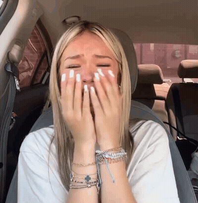 A Woman Sitting In A Car With Her Hands On Her Face GIF