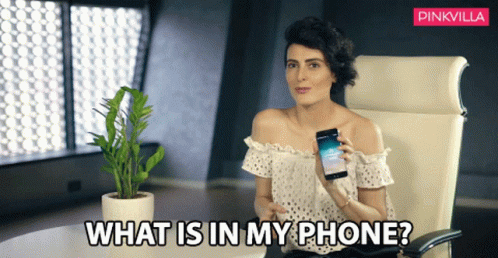 A Woman Sitting In A Chair Holding A Cell Phone With The Words " What Is In My Phone " Above Her GIF