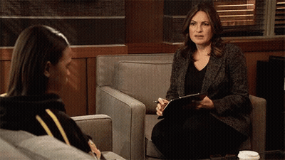 A Woman Sitting In A Chair Talking To Another Woman While Holding A Clipboard GIF