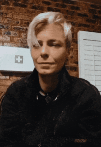 A Woman Sitting In Front Of A Brick Wall With A First Aid Kit In The Background GIF