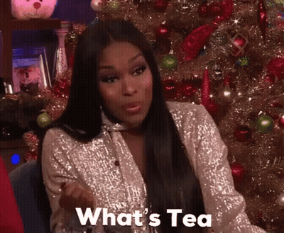 A Woman Sitting In Front Of A Christmas Tree With The Words What 'S Tea Written On Her Face GIF