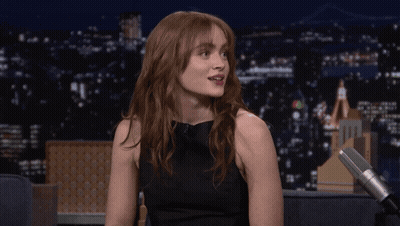 A Woman Sitting In Front Of A Microphone With A City In The Background GIF