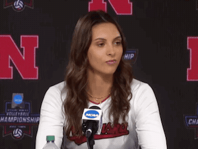 A Woman Sitting In Front Of A Microphone With A Ncaa Logo On Her Shirt GIF