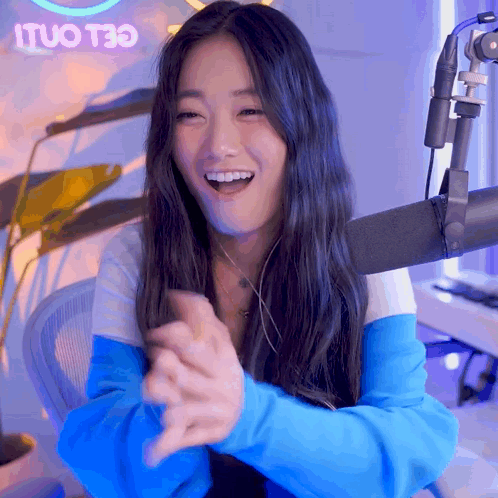 A Woman Sitting In Front Of A Microphone With A Neon Sign That Says Ituo T30 In The Background GIF