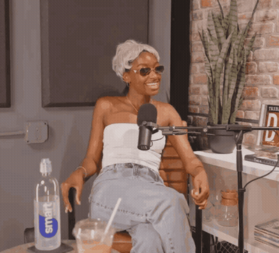 A Woman Sitting In Front Of A Microphone With A Smart Water Bottle Next To Her GIF