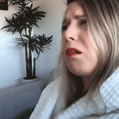 A Woman Sitting In Front Of A Potted Plant Making A Funny Face GIF