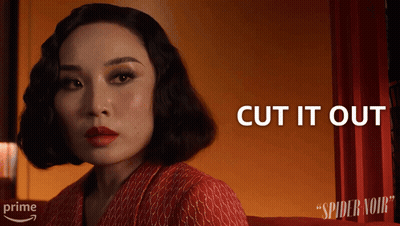 A Woman Sitting In Front Of A Red Curtain With The Words Cut It Out Above Her GIF