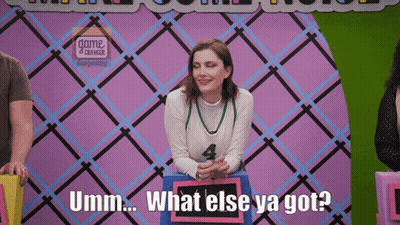 A Woman Sitting In Front Of A Sign That Says What Else Ya Got GIF