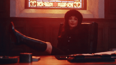 A Woman Sitting In Front Of A Stained Glass Window With Her Feet Up GIF