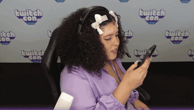 A Woman Sitting In Front Of A Wall That Says ' Twitch Con ' On It GIF