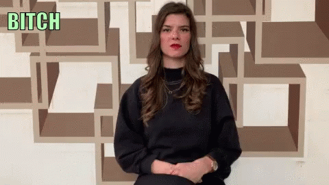 A Woman Sitting In Front Of A Wall With The Word Bitch Written On It GIF