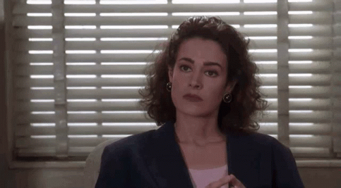 A Woman Sitting In Front Of A Window With Blinds On It . GIF