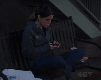 A Woman Sitting On A Bench Looking At Her Phone GIF