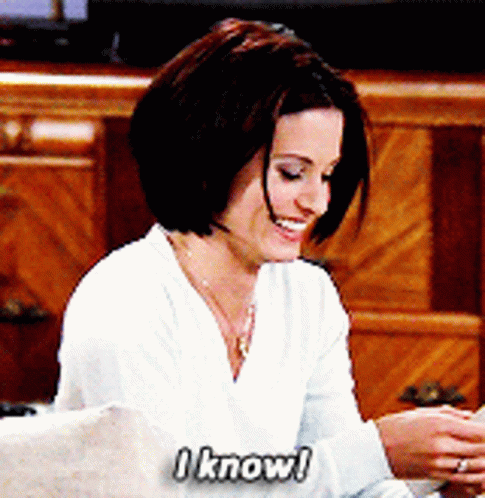 A Woman Sitting On A Couch Says " I Know " While Smiling GIF
