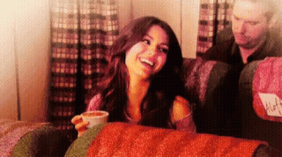 A Woman Sitting On A Couch With A Cup Of Coffee And A Man Behind Her With A Seat Cushion That Says Alfa GIF