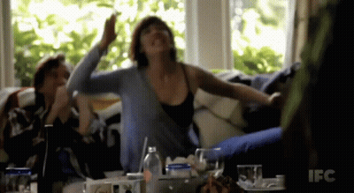 A Woman Sitting On A Couch With Her Arms Outstretched In Front Of A Ifc Sign GIF