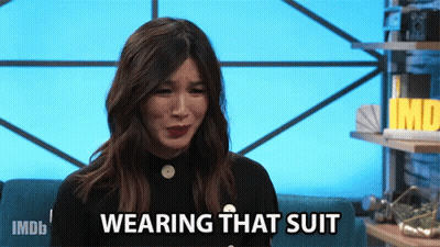 A Woman Sitting On A Couch With The Words " Wearing That Suit " On Her Face GIF