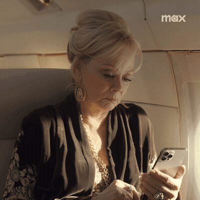 A Woman Sitting On An Airplane Looking At Her Phone With The Max Logo In The Corner GIF