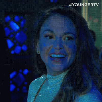 A Woman Smiles And Says " What " In Front Of A Younger Tv Logo GIF