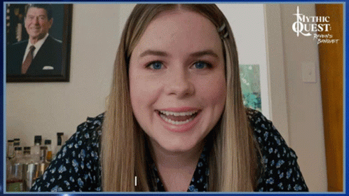 A Woman Smiles In Front Of A Picture Of Ronald Reagan GIF
