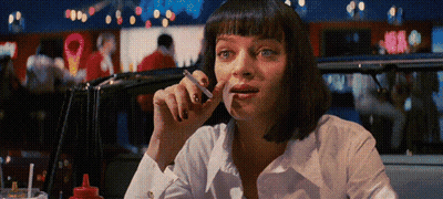 A Woman Smoking A Cigarette In A Diner With A Red Bottle Of Ketchup On The Table GIF