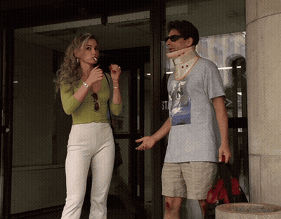 A Woman Smoking A Cigarette Next To A Man With A Collar Around His Neck GIF