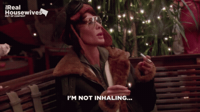 A Woman Smoking A Cigarette With The Words I 'M Not Inhaling Below Her GIF