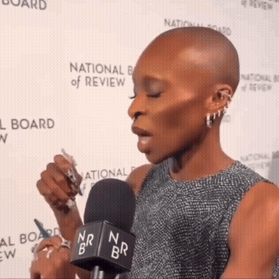 A Woman Speaking Into A Microphone In Front Of A National Board Of Review Wall GIF