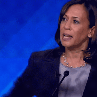 A Woman Speaking Into A Microphone With A Blue Background Behind Her GIF