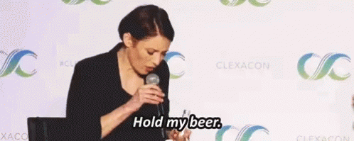 A Woman Speaking Into A Microphone With The Words Hold My Beer Above Her GIF