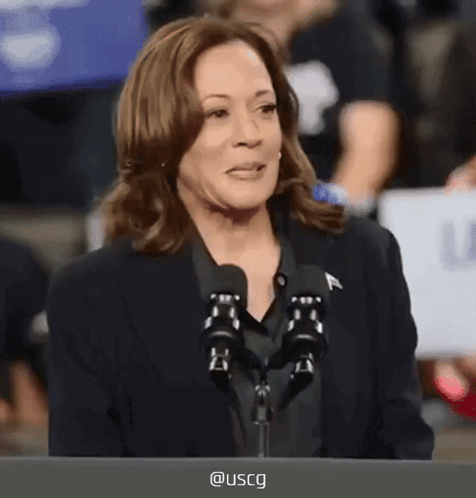 A Woman Speaking Into A Microphone With Uscg Written On The Screen Behind Her GIF