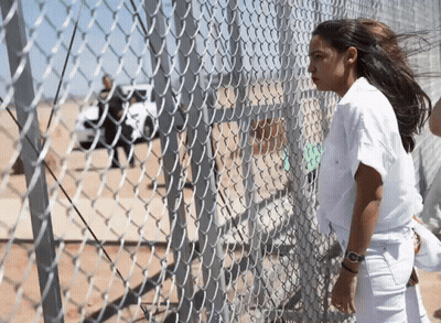 A Woman Standing Behind A Chain Link Fence With A Watch On Her Wrist GIF