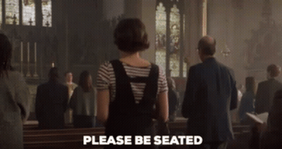 A Woman Standing In A Church With The Words Please Be Seated Written On The Bottom GIF