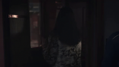 A Woman Standing In A Dark Room Looking Out A Window . GIF