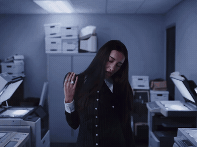 A Woman Standing In A Dark Room With Boxes On The Shelf Behind Her GIF