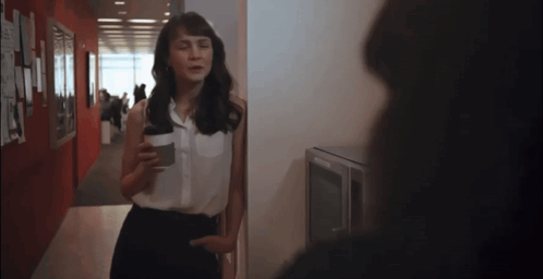 A Woman Standing In A Hallway Holding A Coffee Cup GIF