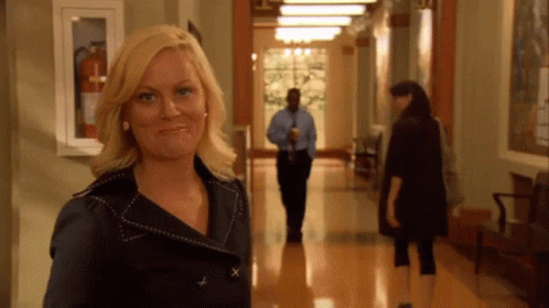 A Woman Standing In A Hallway With A Fire Extinguisher Hanging On The Wall Behind Her GIF