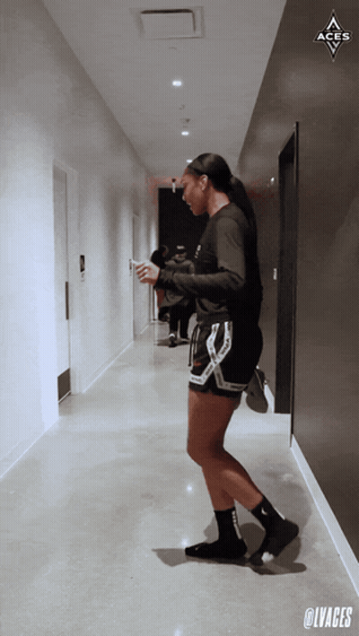 A Woman Standing In A Hallway With The Aces Logo Above Her GIF
