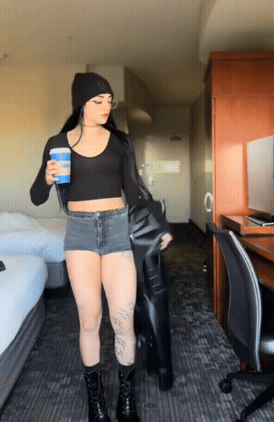 A Woman Standing In A Hotel Room Holding A Cup Of Coffee And A Black Jacket GIF
