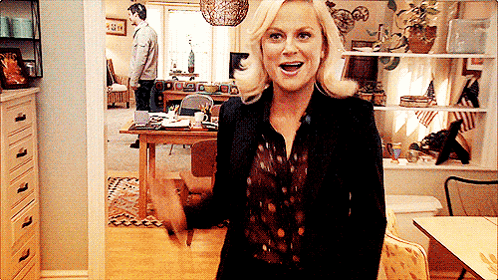 A Woman Standing In A Living Room With A Man Standing In The Background GIF