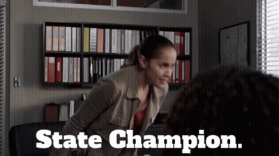 A Woman Standing In Front Of A Bookshelf With The Words State Champion Written On The Bottom GIF