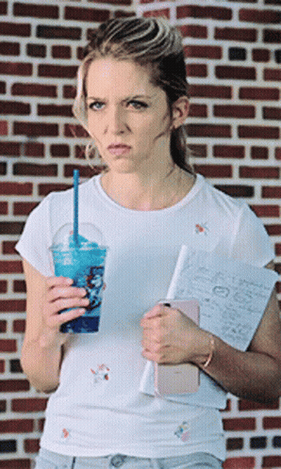 A Woman Standing In Front Of A Brick Wall Holding A Cup Of Blue Liquid GIF
