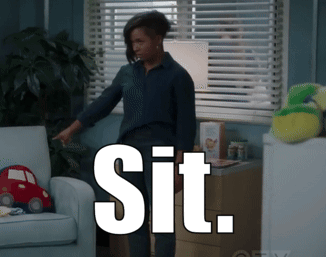 A Woman Standing In Front Of A Couch With The Word Sit On The Bottom GIF