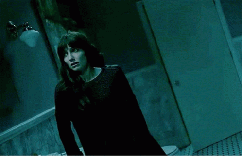 A Woman Standing In Front Of A Mirror In A Dark Room GIF