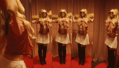 A Woman Standing In Front Of A Mirror Wearing Sunglasses And A Skirt GIF
