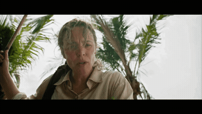 A Woman Standing In Front Of A Palm Tree Holding A Stick GIF
