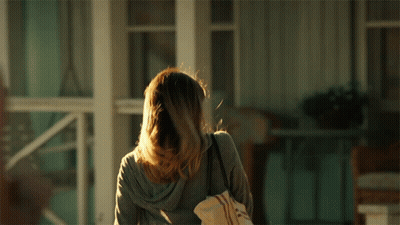 A Woman Standing In Front Of A Porch Holding A Bag GIF